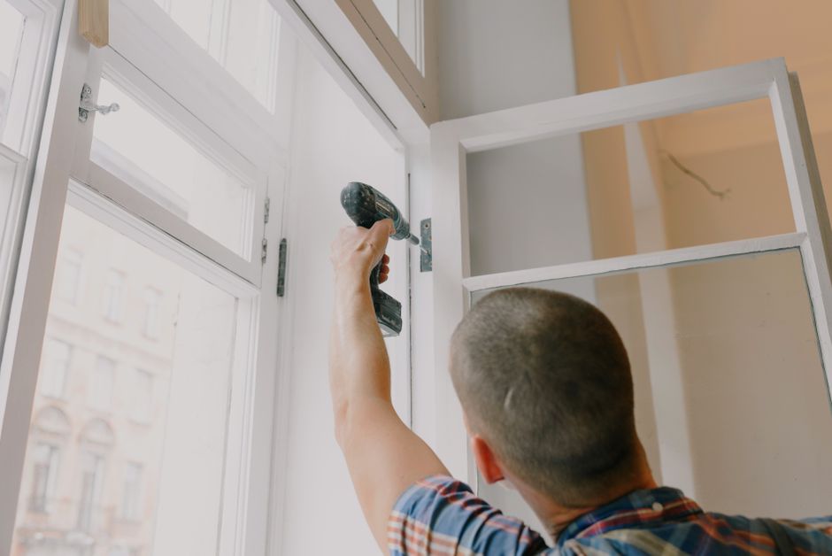 Installer screwing a metal hinge onto a window frame