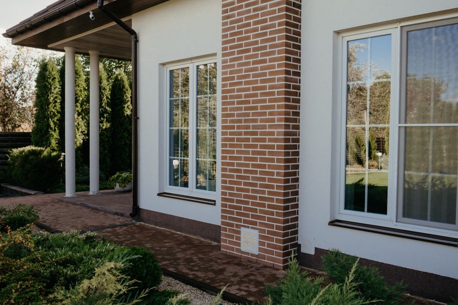 Stylish modern house facade with brick pillar, large glass windows, and lush greenery.
