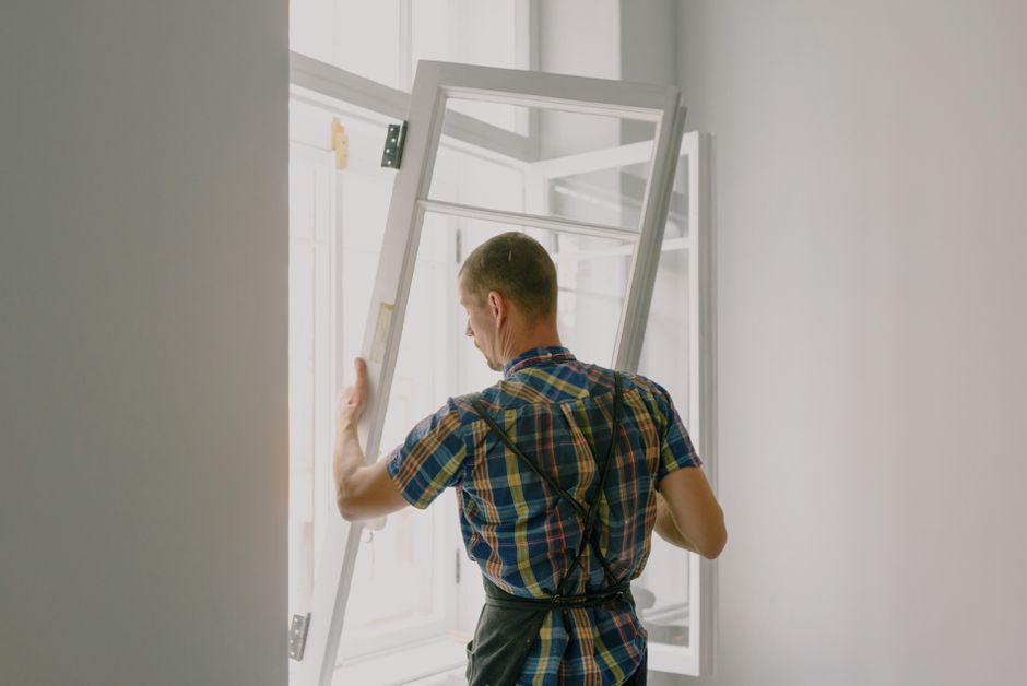 Installer mounting a white window with hinges in a wall opening