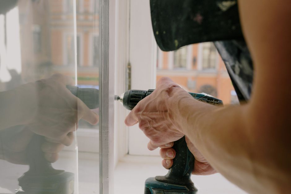 Worker assembling a white window frame with a cordless screwdriver